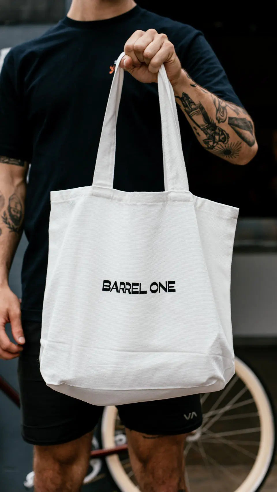 White tote bag with a stylish summer design and the barrel one logo being carried by a person. Stay fashionable and functional this season with our trendy beach tote - perfect for carrying your essentials on a sunny day. 